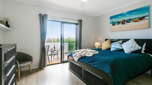 A bedroom with a bed, a desk, a chair, and a balcony with a view. - Fairway 1 - 9/19 Troon Drive (NORMANVILLE)