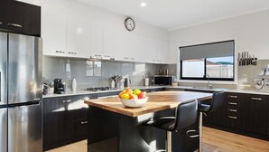 A modern kitchen with a central island, stainless steel appliances, and a view through the window. - Fairway 1 - 9/19 Troon Drive (NORMANVILLE)