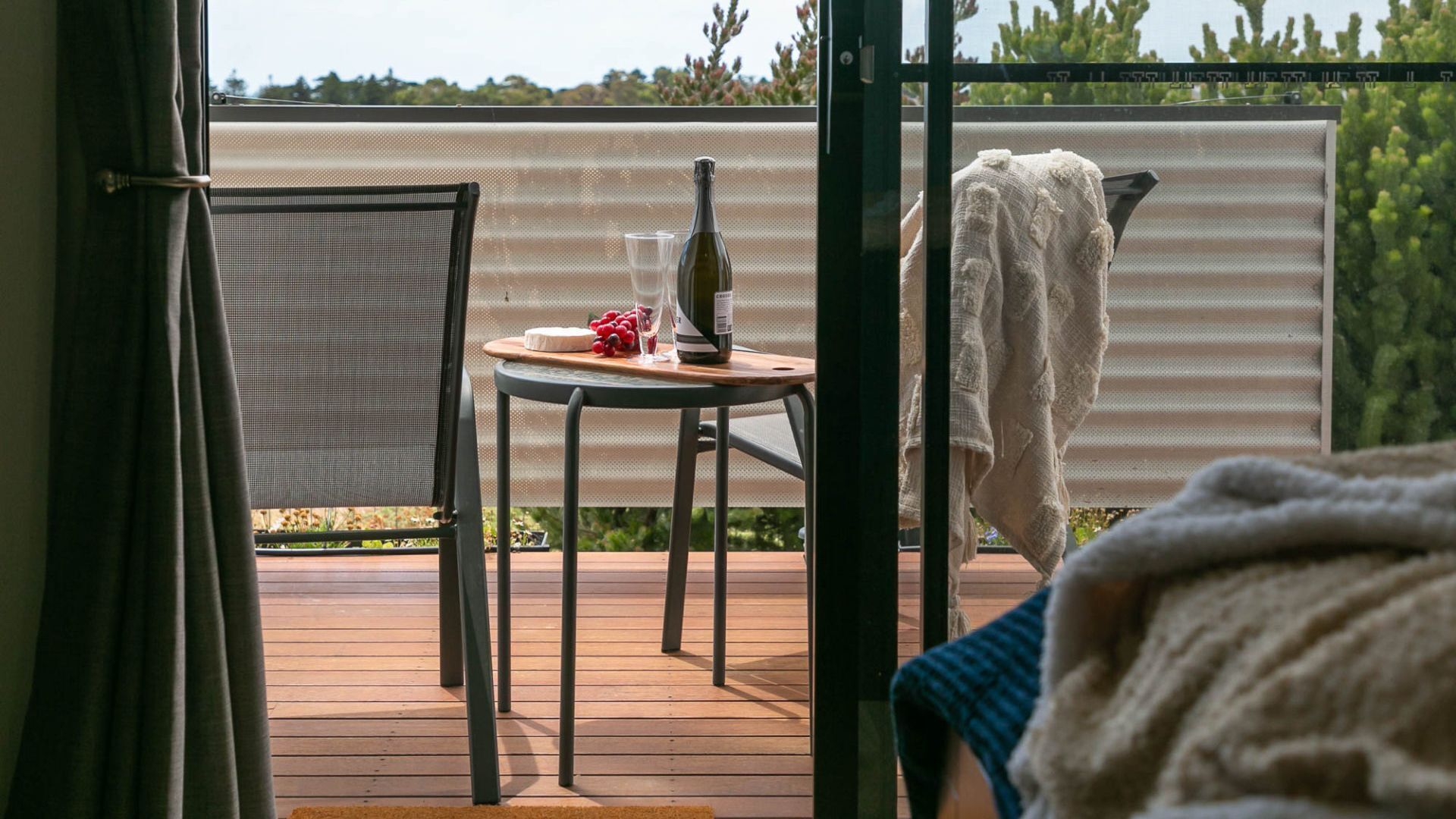 Une terrasse en bois avec une table, une chaise, une bouteille et un verre.