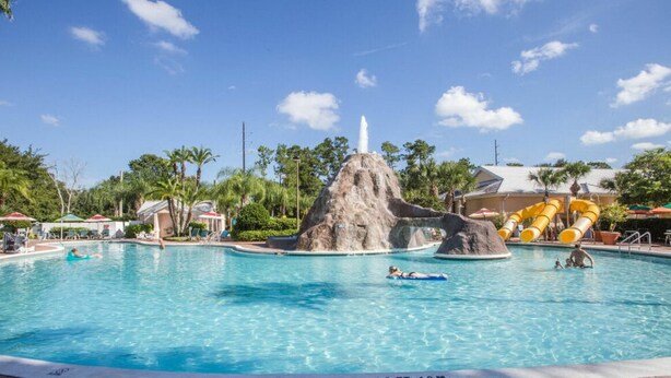 A swimming pool with a rock formation centerpiece, surrounded by palm trees and a water slide. - 2022 Dec23-30 2 BD/2BA 0.8 mi to Disney World at Cypress Pointe Resort (Orlando)