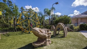 A playground with a yellow climbing structure and dinosaur sculptures on a grassy area. - 2022 Dec23-30 2 BD/2BA 0.8 mi to Disney World at Cypress Pointe Resort (Orlando)