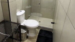Een kleine badkamer met tegels, een toilet, een douchecabine en een metalen prullenbak.