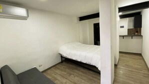 Een kleine, eenvoudig ingerichte kamer met een enkel bed, een tafeltje en een kitchenette.
