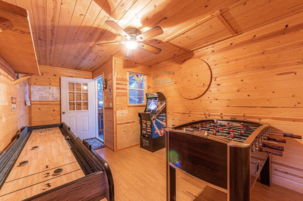 Una stanza con pavimento in legno, un tavolo da calcio, un tavolo da gioco e un bersaglio da freccette.