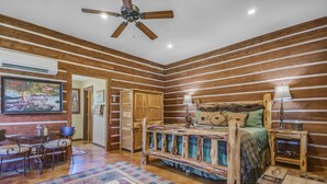 Ein schlafzimmer im Chalet-Stil mit einem Bett, Holzwänden, einem Deckenventilator, einem Teppich und einem Bild an der Wand.