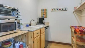 A compact kitchen with a microwave, toaster, and coffee maker. There is a sink and a small shelf with dishes. - San Miguel Suite at Blanco Rapids Ranch (Wimberley)