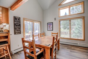A dining area with a wooden table and chairs, large windows, and a kitchen with wooden cabinets. - Royal Aspen Retreat Home: Lovely Setting, Spacious (Breckenridge)