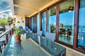 Enjoy ocean views from this balcony with a glass-top table and chairs, a potted plant, and sliding glass door to an outdoor seating area.