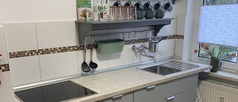 Una cucina moderna con forno a incasso, piano cottura, lavello e una finestra vista alberi.