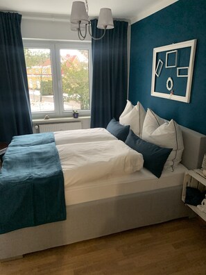 Quarto com cama, janela, cortinas, luminária fixada na parede e um quadro emoldurado.