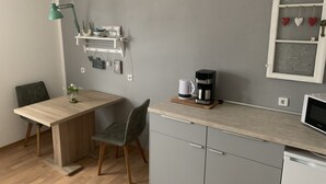 Eine kleine Küche mit Holztisch, einem grünen Stuhl, einer Kaffeemaschine und einem kleinen Regal mit Dekoration.