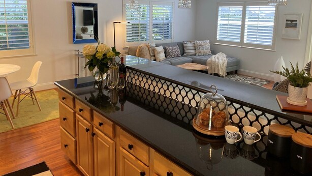 A modern kitchen with a black countertop, wooden cabinets, and a glass-enclosed display case with pastries.