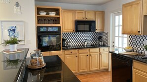 A modern kitchen with wooden cabinets, a black countertop, a microwave, an oven, and a dishwasher.