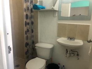 Bathroom features a toilet, sink, and shower area with a shower curtain and a towel storage shelf.