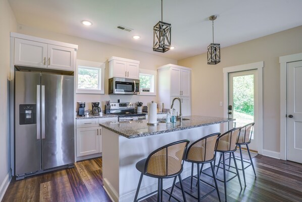 A kitchen with a stainless steel refrigerator, a microwave, and a coffee maker. There are white cabinets and a large island with bar stools. - Wooded Escape w/ Beautiful Backyard + Mtn Views! (Chattanooga)