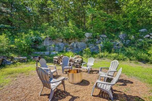 A fire pit surrounded by Adirondack chairs in a natural setting with a stone wall and greenery. - Scenic Mtn Retreat w/ Wooded Backyard + Fire Pit! (Chattanooga)
