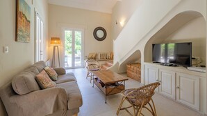 A cozy living room with a sofa, chairs, a wooden table, and a television. - La Tropézienne - Welkeys (Gassin)