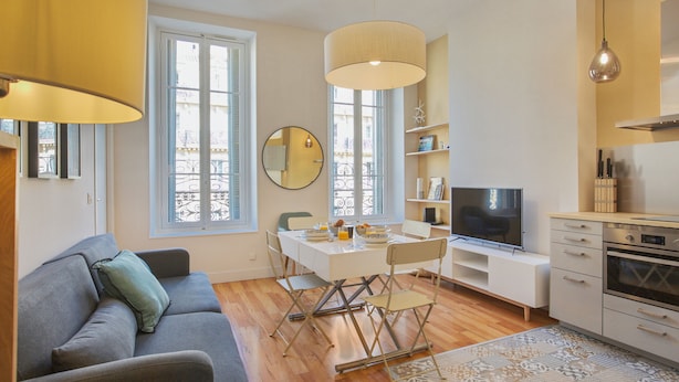 Un apartamento moderno con comedor, sofá, televisor, cocina y ventanas amplias.