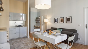 Una cocina moderna con armarios blancos, una mesa de comedor con platos y un sofá gris en la sala.