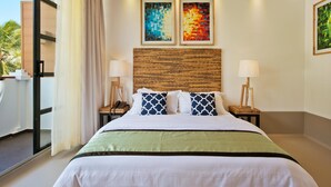 Hotelkamer met een bed, twee schilderijen aan de muur, een geweven hoofdbord en uitzicht op het landschap.