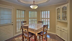 Comedor con mesa, sillas, candelabro y aparador con puertas de vidrio.