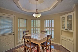 A dining room with a large table, four chairs, a chandelier, and a cabinet with glass doors.