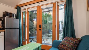 A compact living space with a kitchenette, a sofa with a patterned cushion, and a dining area visible through glass doors.