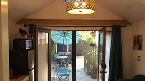 A compact kitchen with a refrigerator, a dining area with a table and chairs, and a view of the backyard through a glass door.