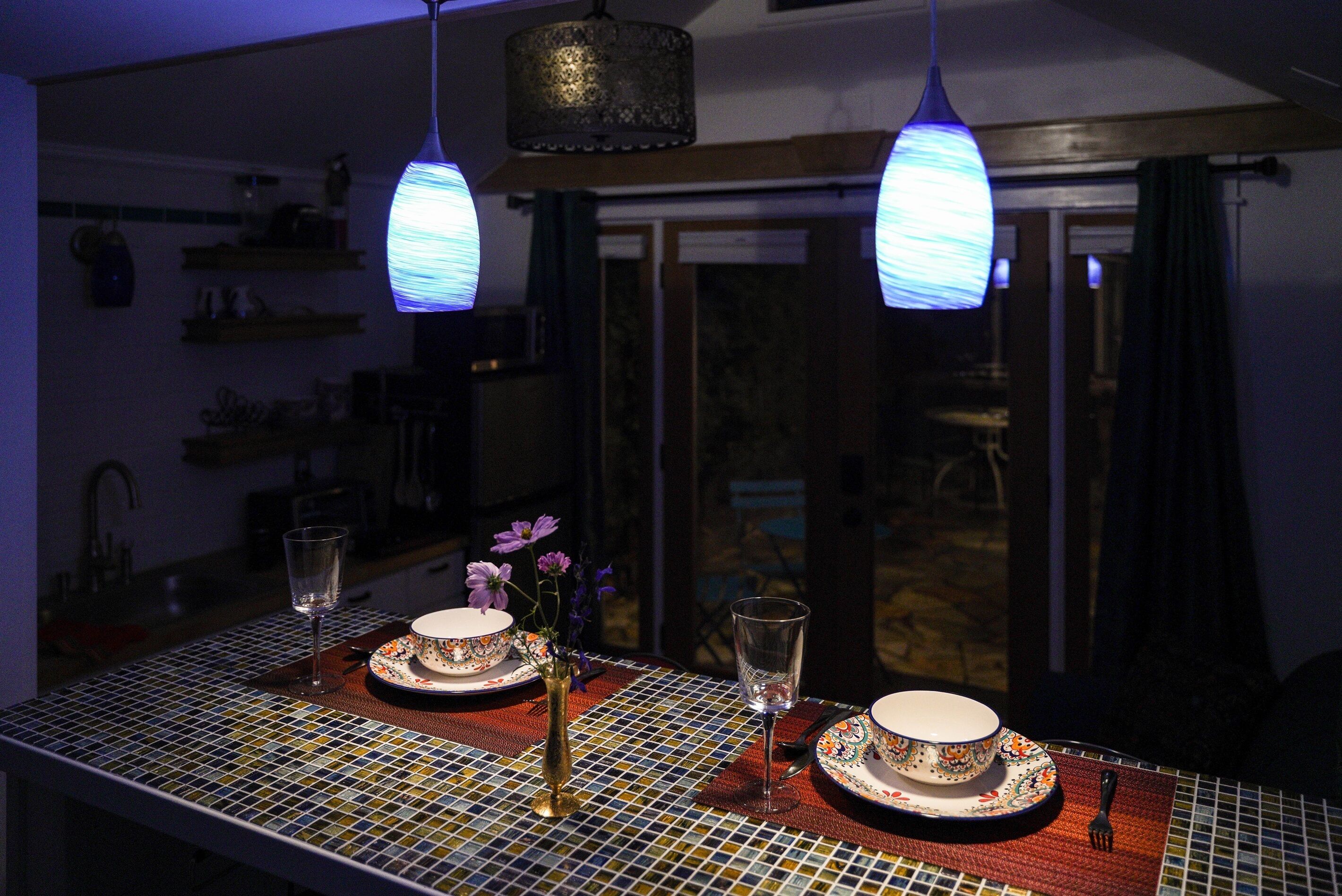 Una mesa de comedor con mantel de mosaico, dos platos, un jarrón con flores y dos vasos.