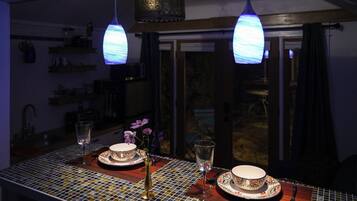 A dining table with a mosaic tablecloth, two plates, a vase with flowers, and two glasses.