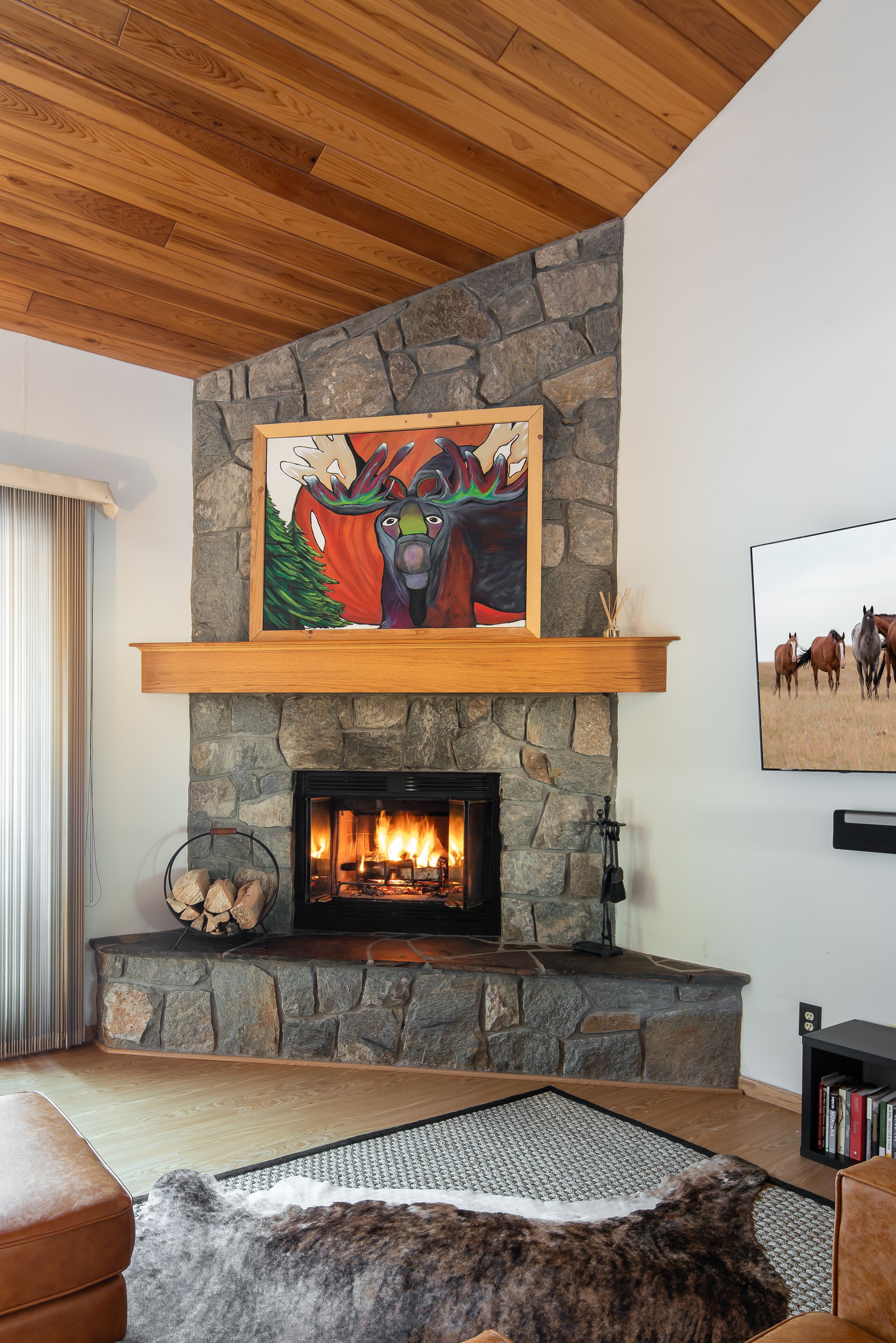 A living room with a stone fireplace, a painting above it, and a fireplace screen.