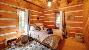 Camera da letto in una baita di legno, con un letto, una ventola a soffitto e una finestra con tende.