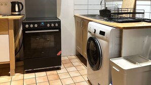 A compact kitchen with a stove, oven, washing machine, and a small countertop.