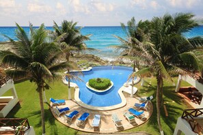 A pool area with lounge chairs and palm trees, overlooking a beach and ocean. - Mi Casa Del Mar B4 - Unwind & rejuvenate in the natural beauty of the Caribbean (Akumal)