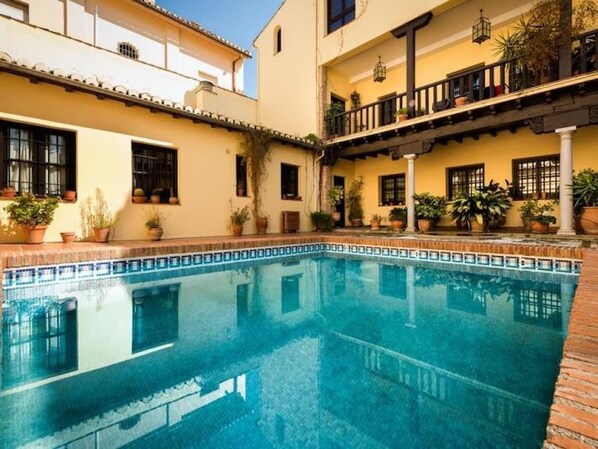 Una piscina con borde de azulejos, rodeada de edificios con balcones y plantas en macetas.