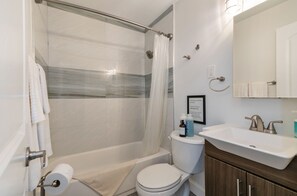 Un baño con ducha, inodoro, lavamanos y un cartel enmarcado en la pared.
