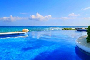 Una piscina azul y cristalina con vista al océano y un promontorio rocoso.
