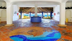 A spacious indoor area with a tiled floor featuring a large mosaic design, a central water feature, and a view of the sea through an open structure with a thatched roof. - Mi Casa Del Mar A6 - Captivating Sea Views from Terrace, Eco-Friendly - No A/C (Akumal)