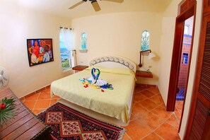 Un dormitorio con una cama, un ventilador, un cuadro y vistas por la ventana.