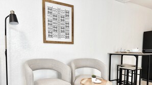 Ein modernes Wohnzimmer mit zwei grauen Sesseln, einem runden Couchtisch mit einer Pflanze, einer schwarzen Stehlampe und einem gerahmten abstrakten Kunstwerk an der Wand.