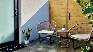 Ein kleiner Sitzbereich im Freien mit Korbstühlen, einem Tisch, einem Blumentopf und einem Holztor.