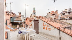 A courtyard with a table and chairs, a small statue, and a building with a clock tower in the background. - GuestHost - Bright apartment, of about 80 sqm with period furniture, which can accommodate up to 4 people, located on the third floor (NO lift) of a typical Venetian building. The building boasts a very central position: it is a two-minute walk from Piaz (Venezia)