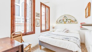 A bedroom with a bed, a desk, a chair, and a window with a view of a building. - GuestHost - Bright apartment, of about 80 sqm with period furniture, which can accommodate up to 4 people, located on the third floor (NO lift) of a typical Venetian building. The building boasts a very central position: it is a two-minute walk from Piaz (Venezia)