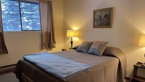 Une chambre à coucher avec un lit, deux lampes de chevet, une fenêtre avec des rideaux et un tableau au mur.