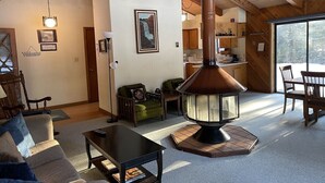 Un salon chaleureux avec un poêle à bois, un canapé, une table basse et un coin repas avec des chaises.