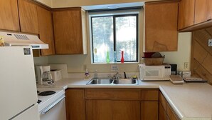 Une cuisine de taille réduite, avec des meubles de rangement en bois, un réfrigérateur blanc, une cuisinière, un four à micro-ondes et un évier.
