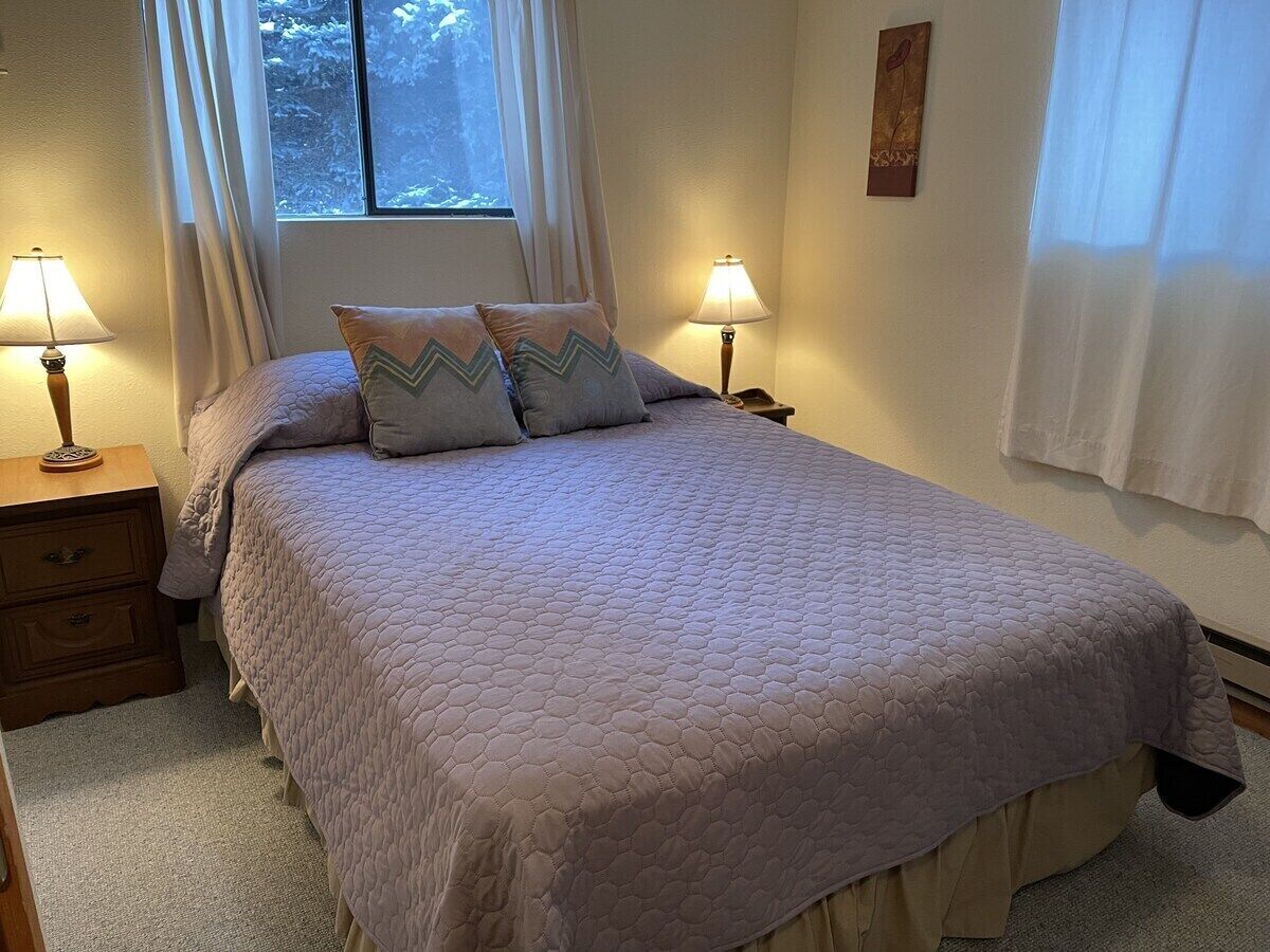 Une chambre à coucher avec un grand lit, deux tables de chevet, une fenêtre avec des rideaux et une œuvre d’art accrochée au mur.
