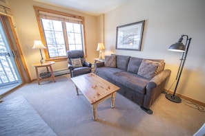 A cozy living room with a wooden coffee table, a grey sofa, and a chair. There are two lamps on side tables, and a framed picture on the wall. - Scenic Summer Stay | Outdoor Pool, Village Action (Keystone)