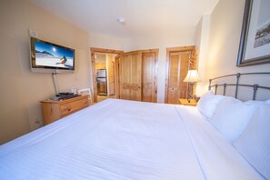 Une chambre d’hôtel avec un grand lit, un téléviseur fixé au mur, des portes en bois et une table de chevet avec une lampe.
