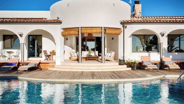 A poolside area with lounge chairs, a wooden deck, and a covered seating area with a view of the pool.